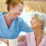 A caregiver and client smile while the caregiver hugs and helps the client, representing professional caregiving.