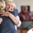 An older woman smiles as a younger woman visits her and hugs her, showing the effect that acts of kindness can have on senior loved ones.