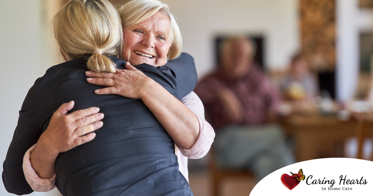 An older woman smiles as a younger woman visits her and hugs her, showing the effect that acts of kindness can have on senior loved ones.