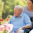 A caregiver brings an older adult with a wheelchair to see some flowers representing how professional caregivers can make outdoor activities accessible.